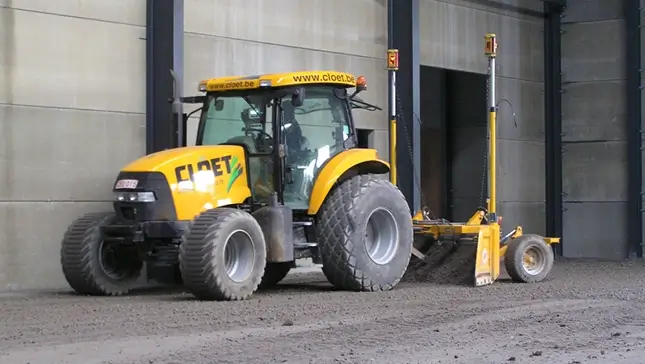 Tractor met nivelleerbak van Cloet bij een bedrijfshal